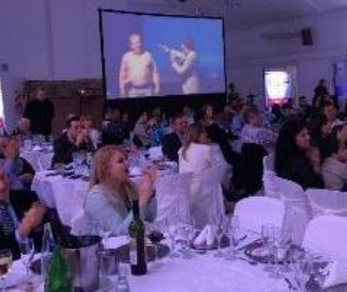 Show en un salón con pantalla gigante y el público en mesas